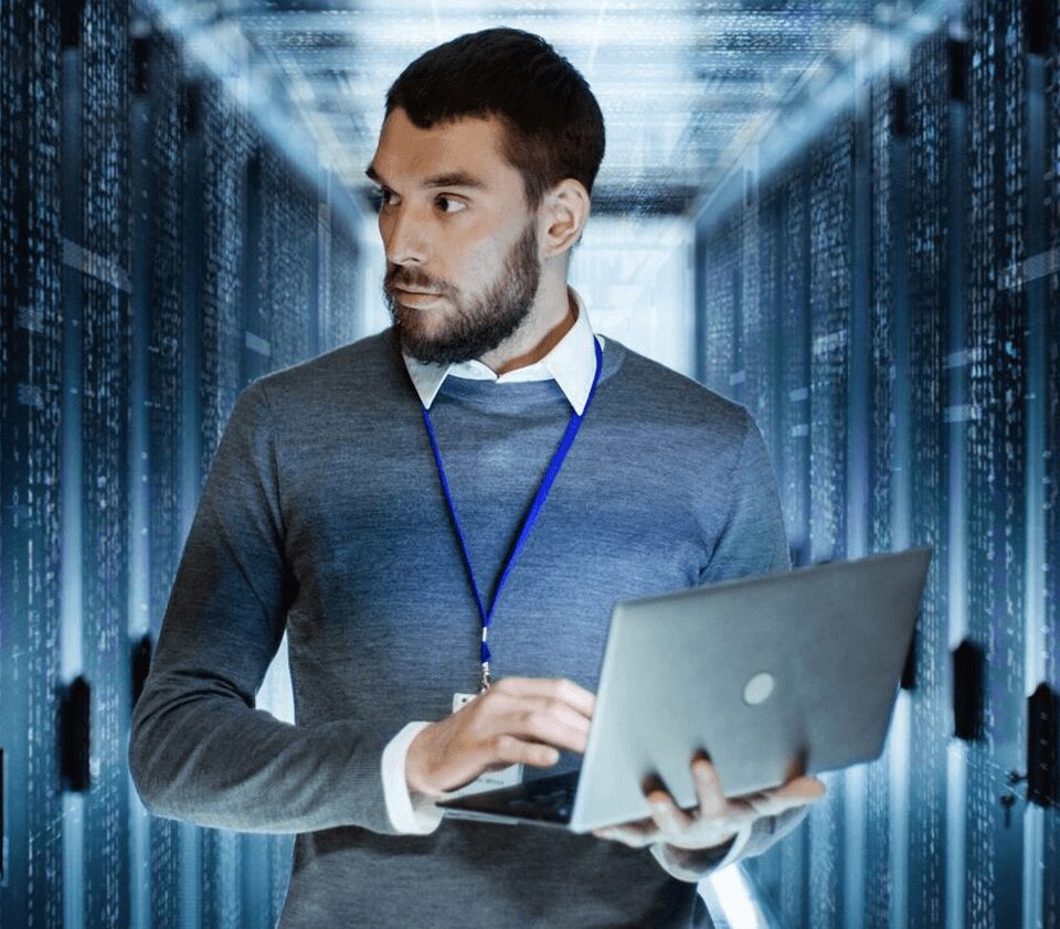 A man holding a laptop in front of some servers.